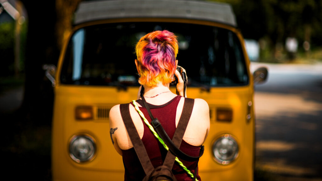 Kay stands, facing away from the camera and towards a yellow Volkswagen bus.