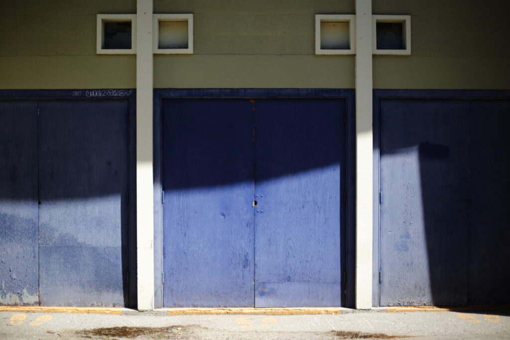 A row of blue, handless doors separated by concrete columns.