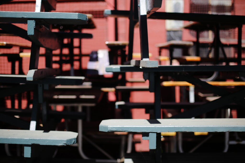 Old, blue painted wood picnic tables stacked in front of a red brick wall.