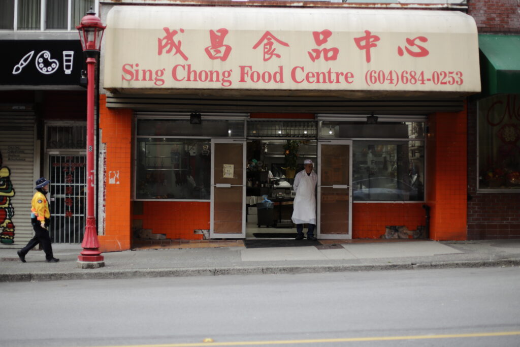 A man in an apron stands in the entrance of a Chinese meat shop.