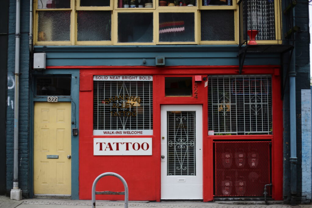 A yellow door next to the bright red entrance to a tattoo shop advertising "Walk-ins Welcome."