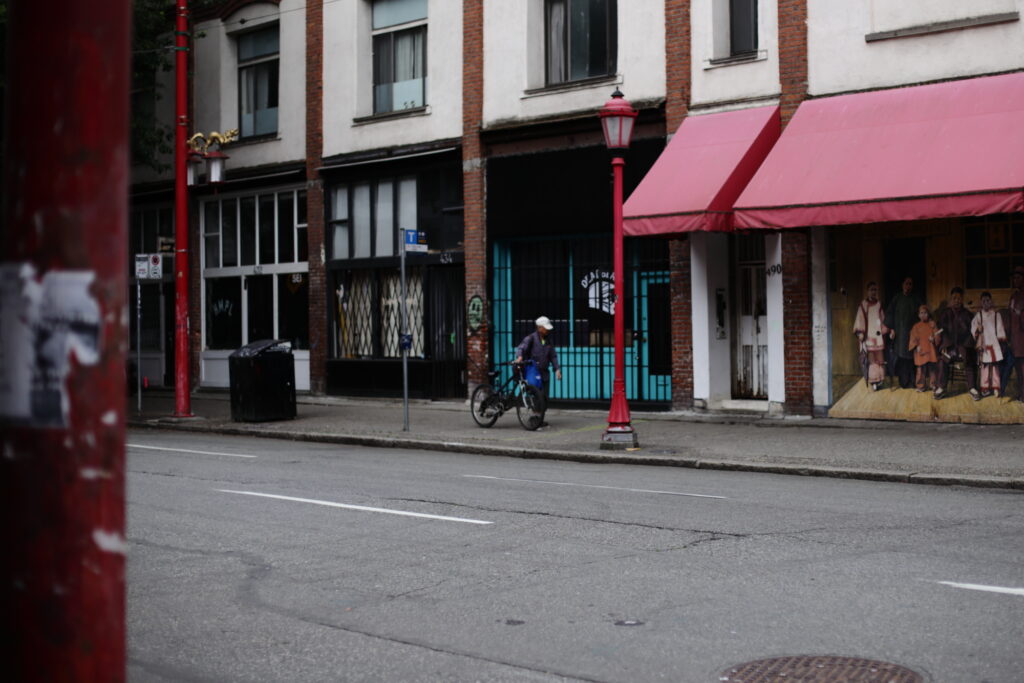 A man walks with his bicycle down an otherwise empty street lined with closed businesses.