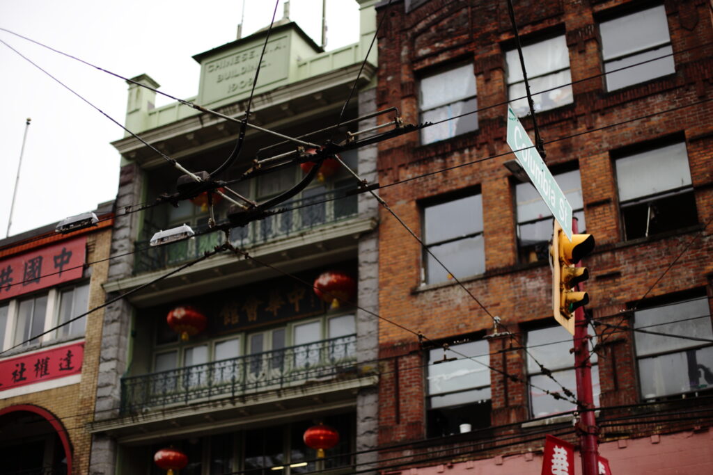 Electric trolly bus lines criss cross the foreground of a photo of three buildings in Vancouver's Chinatown.